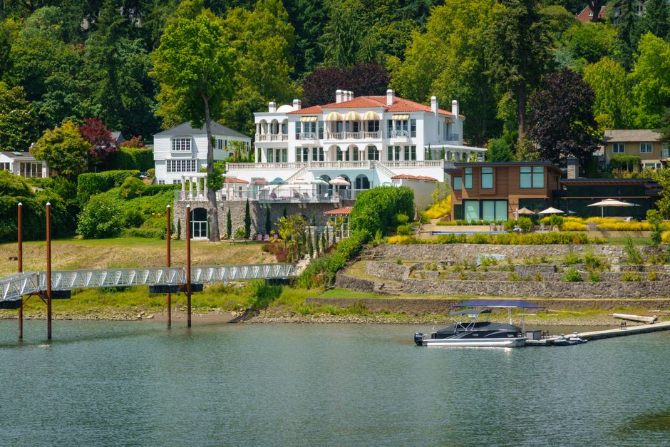 An aerial view of a luxurious waterfront property featuring a private boat dock extending into the clear blue water, with a boat tied up.