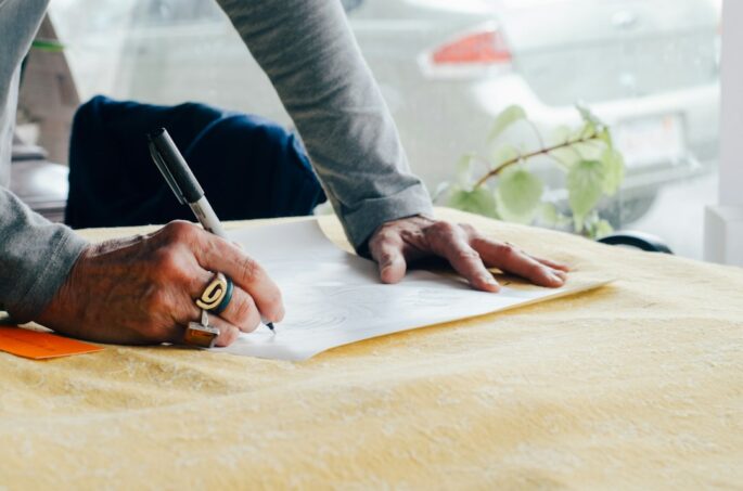 Close-up, brightly lit photo of a person's hands using a professional pen to sign a real estate document, symbolizing the ...