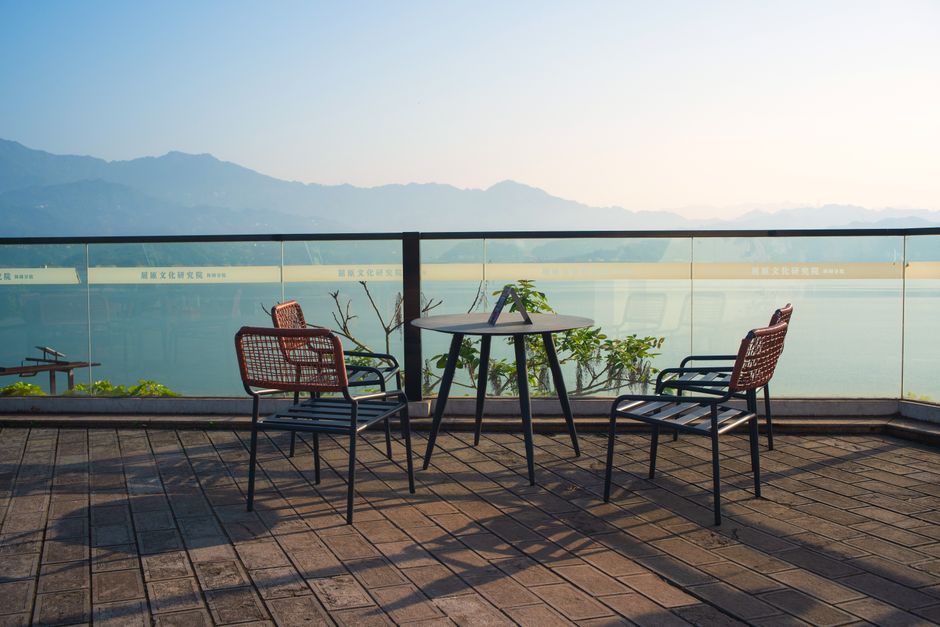 Two empty chairs on a wooden deck of a waterfront home, offering a peaceful and serene view of a wide river at sunrise.