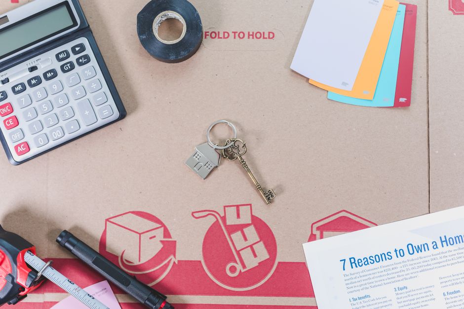 A person holds a small calculator in one hand and a set of house keys in the other, representing the financial calculations involved in selling a home.